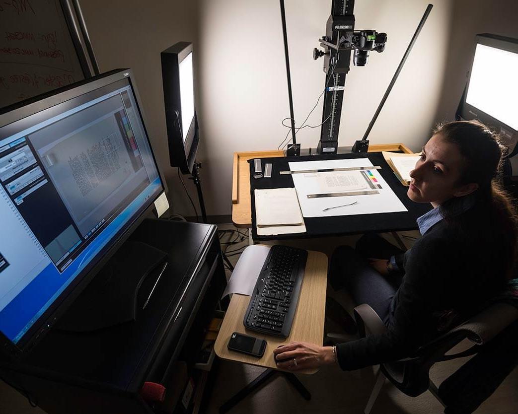 Researcher working on digitizing printed materials with a computer display in the background